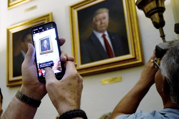 FILE - In this Aug. 1, 2019 file photo, people take photos of President Donald Trump's portrait hanging in the Colorado Capitol after an unveiling ceremony in Denver. On Friday, Aug. 9, 2019, The Associated Press reported on a manipulated video circulating online incorrectly asserting that the painting of Obama, left, fell off the wall as Trump’s was unveiled. (AP Photo/Thomas Peipert)
