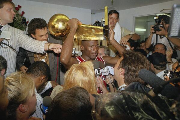 FILE - Chicago Bulls Michael Jordan holds the NBA Championship trophy aloft while talking with the media in the locker room after their 108-101 win against the Los Angeles Lakers at Inglewood, Calif., June 13, 1991. (AP Photo/Reed Saxon, File)