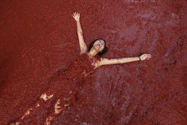 A woman reacts during the annual tomato fight fiesta called "Tomatina" in the village of Bunol near Valencia, Spain, Wednesday, Aug. 30, 2023. Thousands gather in this eastern Spanish town for the annual street tomato battle that leaves the streets and participants drenched in red pulp from 120,000 kilos of tomatoes. (AP Photo/Alberto Saiz)