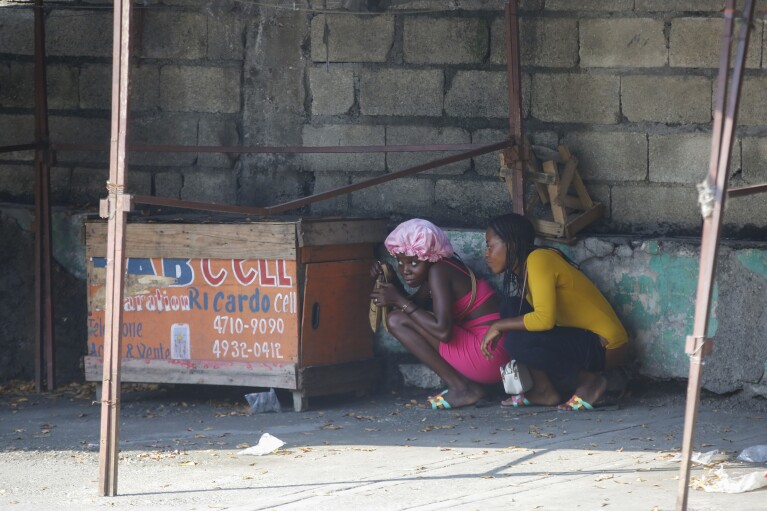 Women take cover during a gun battle between police and gang members in Port-au-Prince, Haiti, Friday, March 1, 2024. (AP Photo/Odelyn Joseph)