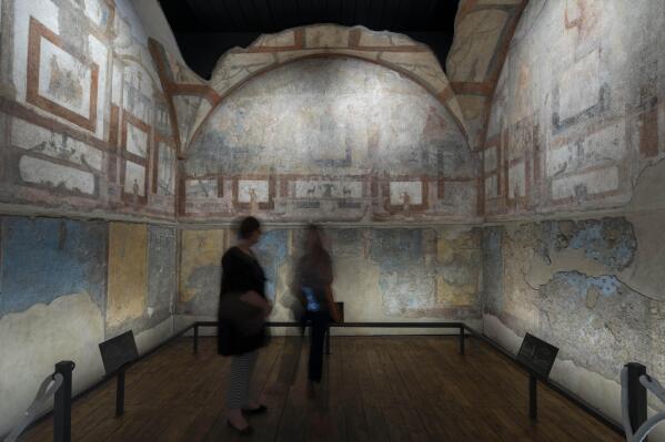 Journalists look at the frescoes coming from the sacellum, a small votive chapel, of a two-story home, or "Domus," dating from around 134-138 AD that was partially destroyed to make way for the construction of the Caracalla public baths, which opened in 216 AD, are on display at the Caracalla archaeological park in Rome, Thursday, June 23, 2022. The frescoed ceiling and walls of a domestic temple honoring Greco-Roman and Egyptian religious deities and believed to have belonged to a wealthy merchant family were first discovered in the mid-19th century about 10 meters (yards) underneath the current ground level of the baths, had been briefly exhibited but has been closed to the public for 30 years. (AP Photo/Domenico Stinellis)