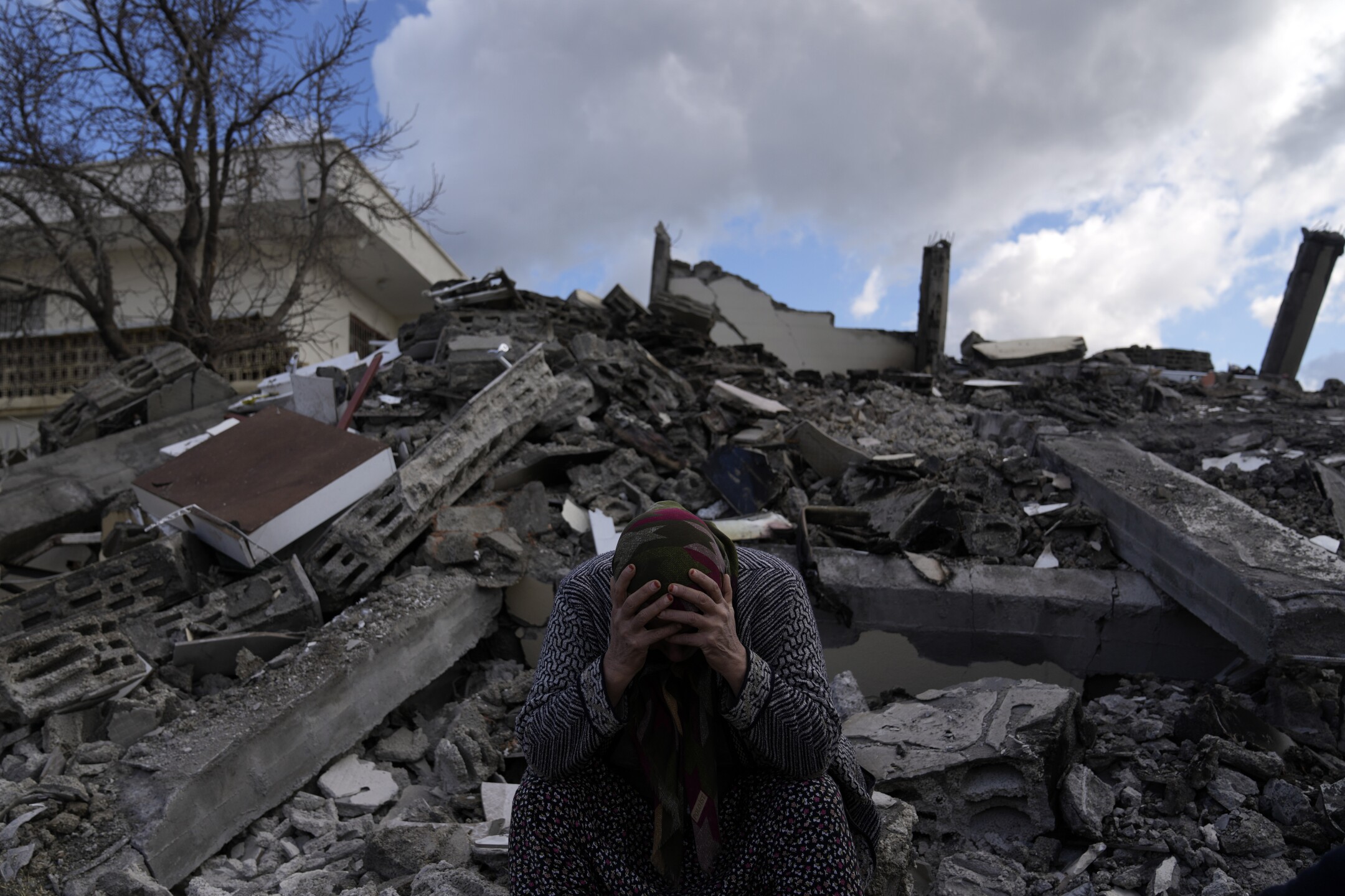 A woman sits on the rubble as emergency rescue teams search for people under the remains of destroyed buildings in Nurdagi town on the outskirts of Osmaniye, Turkey, on Feb. 7, 2023, the day after a powerful earthquake hit southeast Turkey and Syria. (AP Photo/Khalil Hamra)