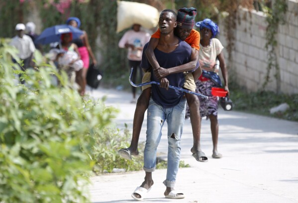 Un residente lleva a un anciano a la espalda mientras huye de su casa para evitar enfrentamientos entre bandas armadas en el distrito Bernier de Pétion-Ville, Haití, el miércoles 31 de enero de 2024. (Foto AP/Odelyn Joseph)