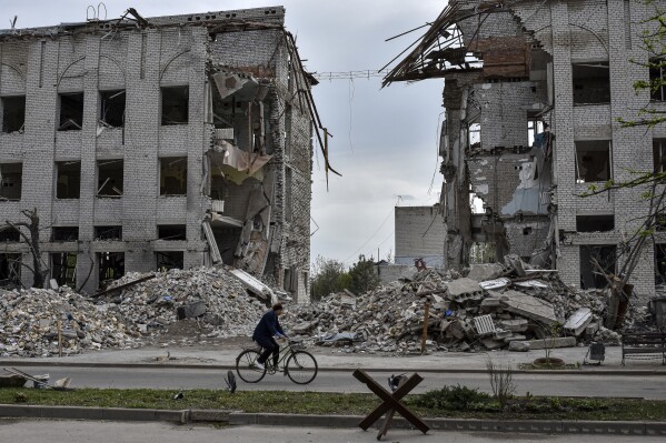 A local woman rides a bicycle on April 18, 2024, in front of a building destroyed by a Russian airstrike in the frontline town of Orikhiv, Ukraine. (AP Photo/Andriy Andriyenko, File)