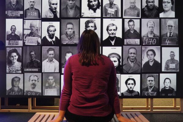 A member staff watches a digital display showcasing the identification photographs of British prisoners of war held abroad and foreign internees held in Britain, part of the Great Escapes: Remarkable Second World War Captives exhibition at the National Archives, in Kew, Richmond, England, Tuesday, Jan. 30, 2024. A new exhibit that opened Friday Feb. 2, 2024 at The National Archives in London uses the 80th anniversary of the so-called Great Escape by allied airmen from a German prisoner of war camp to explore escapes by captives of all kinds during World War II. (Jonathan Brady/PA via AP)