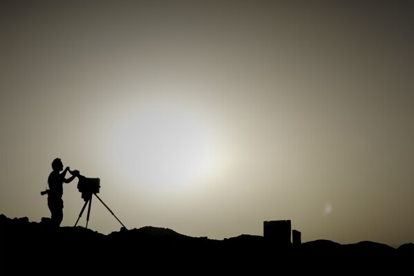 Associated Press photographer Rodrigo Abd takes a photo with a wooden box camera at a former U.S. base in the Arghandab Valley of Afghanistan, June 11, 2023. The kamra-e-faroee, or “instant camera,” is a handmade box on a tripod that combines a simple camera and darkroom in one. (AP Photo/Bram Janssen)