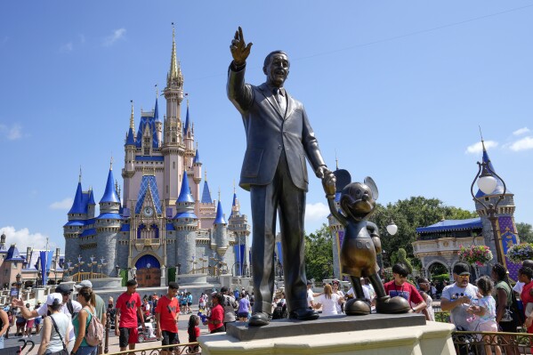 Visitantes del parque temático Magic Kingdom caminan cerca de una estatua de Walt Disney y Mickey Mouse, el viernes 14 de julio de 2023, en Lake Buena Vista, Florida. (AP Foto/John Raoux)
