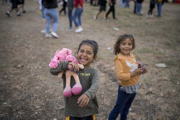 A little girl laughs clutching a doll at a fair in Hagioaica, Romania, Saturday, Sept. 16, 2023. For many families in poorer areas of the country, Romania's autumn fairs, like the Titu Fair, are one of the very few still affordable entertainment events of the year. (AP Photo/Vadim Ghirda)