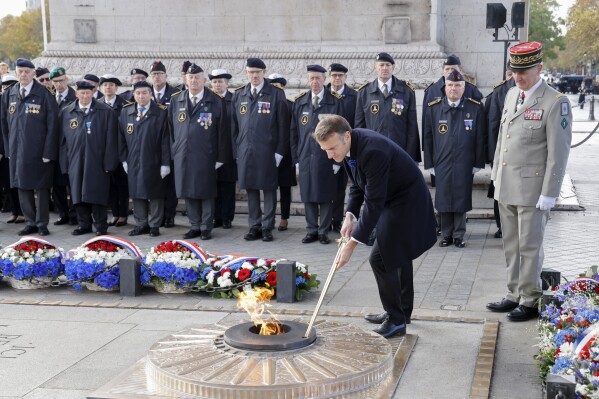 French President Emmanuel Macron adjusts the flame at the Tomb of the Unknown Soldier during a ceremony at the Arc de Triomphe, as part of the commemorations marking the105th anniversary of the Nov. 11, 1918 Armistice, ending World War I, Saturday, Nov. 11, 2023 in Paris. (Ludovic Marin/Pool via AP)