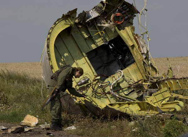 FILE - In this July 22, 2014 file photo, a pro-Russian rebel touches the MH17 wreckage at the crash site of Malaysia Airlines Flight 17, near the village of Hrabove, eastern Ukraine.  Five years after a missile blew Malaysia Airlines Flight 17 out of the sky above eastern Ukraine, relatives and friends of those killed are gathering Wednesday July 17, 2019, at a Dutch memorial to mark the anniversary. (AP Photo/Vadim Ghirda, File)
