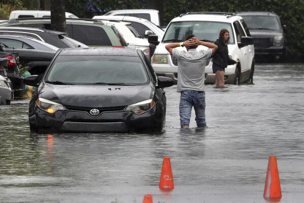 A driver climbs out of his stalled car after he tried to move it to higher ground from the flooded parking lot at the Beachwalk at Sheridan Apartments in Dania Beach, Fla., on Saturday, June 4, 2022. (Mike Stocker/South Florida Sun-Sentinel via AP)
