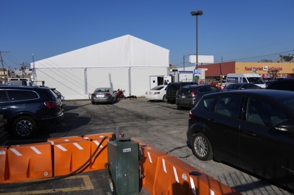 Varios automóviles permanecen estacionados junto a una carpa para albergar a migrantes en el estacionamiento de una vieja tienda CVS, el jueves 1 de febrero de 2024, en el vecindario Little Village de Chicago. (AP Foto/Erin Hooley)