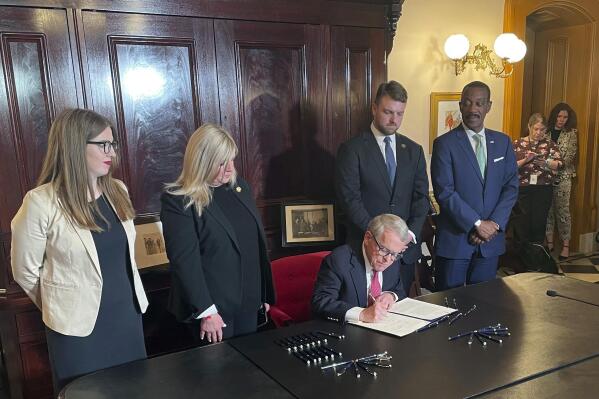 Ohio Gov. Mike DeWine, flanked by state lawmakers from both sides of the aisle, signs Ohio's transportation budget into law at the statehouse, Friday, March 31, 2023, in in Columbus, Ohio. The measure includes railway safety provisions in response to February's East Palestine train derailment and toxic chemical spill. (AP Photo/Samantha Hendrickson)