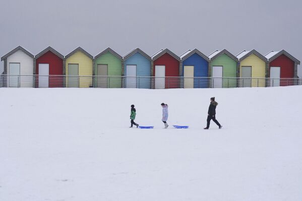 People walk through the snow beside the beach huts at Blyth in Northumberland, England, Sunday, Dec. 3, 2023 as temperatures are tipped to plunge to as low as minus 11C (12.2 F) in parts of the UK over the weekend. (Owen Humphreys/PA via AP)