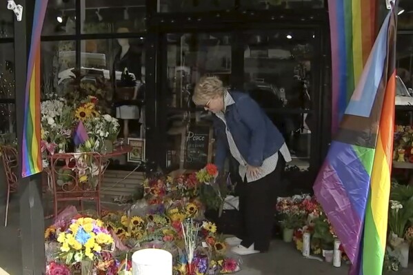 In this image taken from KABC7 Los Angeles video, a woman drops off flowers at a makeshift memorial outside the Mag.Pi store in Cedar Glen, Calif., Monday, Aug. 21, 2023. Authorities say a 27-year-old man killed by California sheriff's deputies after he fatally shot a store owner on Friday, Aug. 18, 2023, had ripped down an LGBTQ+ Pride flag outside the business and shouted homophobic slurs at the woman. Laura Ann Carleton was pronounced dead at Mag.Pi, the store she owned and operated in Cedar Glen. (KABC7 Los Angeles via AP)