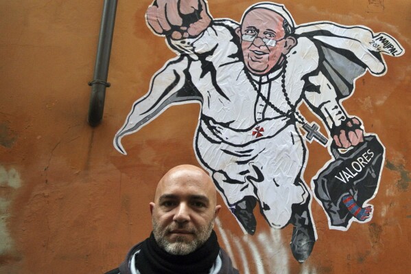 FILE - Italian artist Mauro Pallotta poses in front of his graffiti depicting Pope Francis as Superman and holding a bag with a writing which reads: 