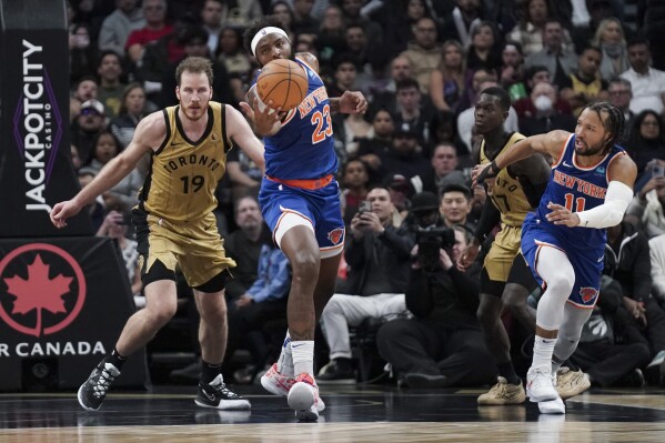 New York Knicks center Mitchell Robinson (23) rebounds the ball while being pursued by Toronto Raptors center Jakob Poeltl (19) during second-half NBA basketball game action in Toronto, Friday, Dec. 1, 2023. (Arlyn McAdorey/The Canadian Press via AP)