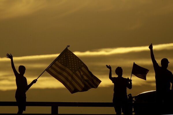 People wave to passing motorists below to commemorate the anniversary of the Sept. 11 terrorist attacks from an overpass on Interstate 35 Wednesday, Sept. 11, 2019, near Melvern, Kan. Area residents began manning the bridge with flags and waving to motorists on the anniversary in 2002 and have done it ever since. (AP Photo/Charlie Riedel)