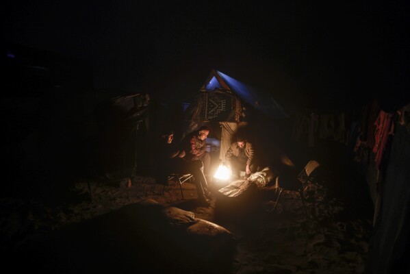 Palestinians displaced by the Israeli ground offensive on the Gaza Strip sit by a fire at a makeshift tent camp in Rafah, Gaza Strip, Sunday, Feb. 18, 2024. (AP Photo/Mohammed Dahman)