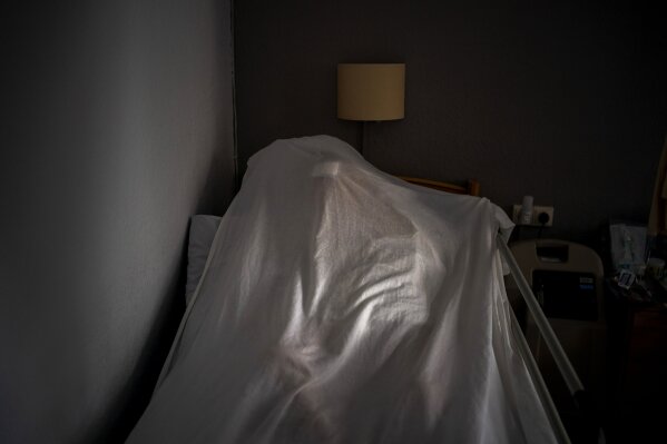 The body of an elderly person who died of COVID-19 is covered with a sheet on a bed in a nursing home in Barcelona, Spain, Friday, Nov. 13, 2020. Like doctors and nurses, mortuary workers are part of a group of essential workers who see and touch the daily march of death amid the worst public health crisis in over a century. (AP Photo/Emilio Morenatti)