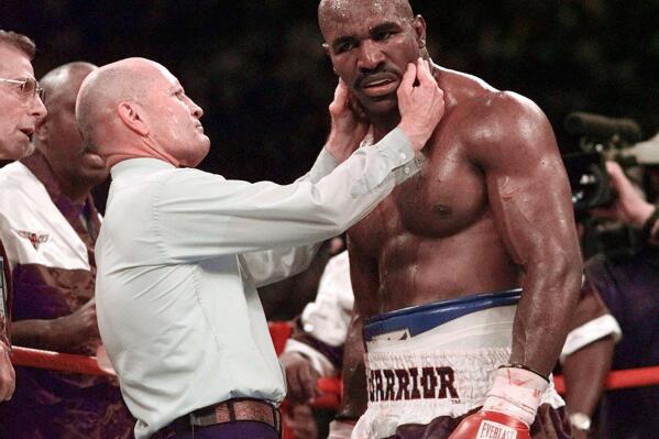 FILE - Evander Holyfield has his right ear checked by referee Mills Lane after he was bit on the ear by Mike Tyson during the third round of their WBA heavyweight boxing match June 28, 1997, in Las Vegas. Lane, the Hall of Fame boxing referee who was the third man in the ring when Tyson bit Holyfield’s ear, died Tuesday, Dec. 6, 2022. He was 85. Lane had suffered a stroke in 2002 and son Tommy said his father had taken a significant turn for the worse recently before entering hospice care Friday. (AP Photo/Mark J. Terrill, File)
