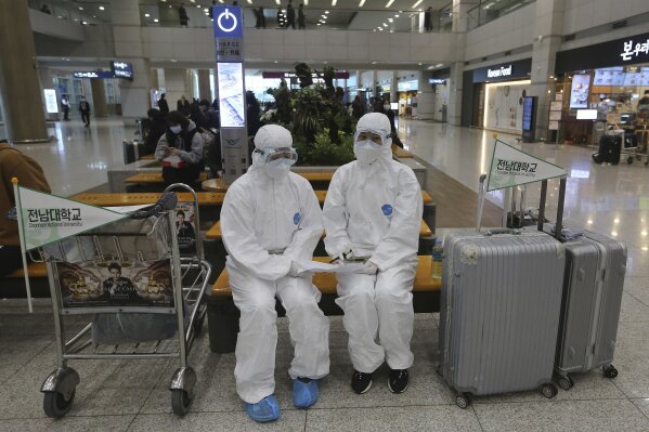 Chonnam National University staff wearing protective attire are on standby for special transportation for Chinese students studying at their university, at Incheon International Airport in Incheon, South Korea, Tuesday, Feb. 25, 2020. Chinese students of the university are to arrive from China after their holiday. China and South Korea on Tuesday reported more cases of a new viral illness that has been concentrated in North Asia but is causing global worry as clusters grow in the Middle East and Europe. (AP Photo/Ahn Young-joon)