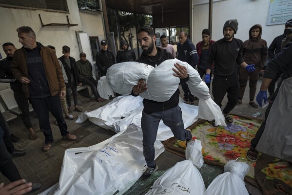 A Palestinian man carries the body of his relative killed in the Israeli bombardment of the Gaza Strip, outside a morgue in Rafah, southern Gaza, Friday, Dec. 29, 2023. (AP Photo/Fatima Shbair)