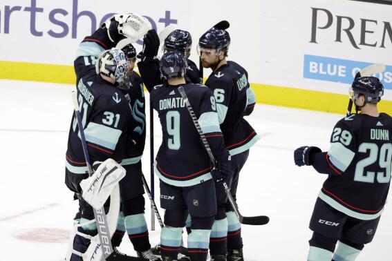 Seattle Kraken players, including goaltender Philipp Grubauer (31), center Ryan Donato (9) defenseman Adam Larsson (6) and defenseman Vince Dunn (29), celebrate the the team's shootout win over the New Jersey Devils in an NHL hockey game Saturday, April 16, 2022, in Seattle. (AP Photo/John Froschauer)