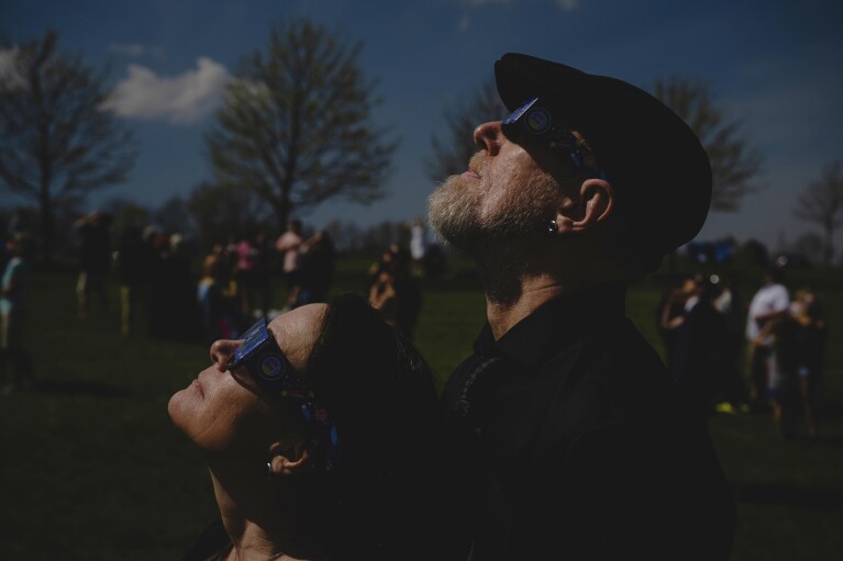 A newly-wed couple looks up at a total solar eclipse during a mass wedding ceremony at Trenton Community Park, Monday, April 8, 2024, in Trenton, Ohio. (AP Photo/Jon Cherry)