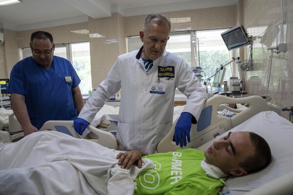 Chief Doctor Serhii Ryzhenko speaks to a Oleh Halah, 22, Ukrainian soldier, injured by a Russian tank near Lyman, at Mechnikov Hospital in Dnipro, Ukraine, Friday, July 14, 2023. A surge of wounded soldiers has coincided with the major counteroffensive Ukraine launched last month to try to recapture its land from Russian forces. Surgeons at Mechnikov Hospital, one of the country's biggest, are busier now than perhaps at any other time since Russia began its invasion 17 months ago. (AP Photo/Evgeniy Maloletka)