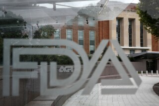 FILE - A U.S. Food and Drug Administration building is seen behind FDA logos at a bus stop on the agency's campus in Silver Spring, Md., on Aug. 2, 2018. Federal health advisers voted against an experimental treatment for Lou Gehrig’s disease at a Wednesday, Sept. 27, 2023, meeting prompted by years of patient efforts seeking access to the unproven therapy. (AP Photo/Jacquelyn Martin, File)