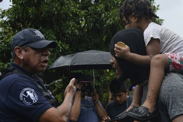 A federal police officer, left, speaks to a migrant carrying a child, right, near Tuzantan, Chiapas state, Mexico, Saturday, Oct. 12, 2019. Hundreds of migrants were arrested by Mexican authorities as they made their way to Mexico City. (AP Photo/Isabel Mateos)