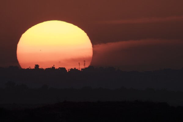 The sun sets behind the buildings in the Gaza Strip as seen from southern Israel, Tuesday, Jan. 16, 2024. (AP Photo/Leo Correa)