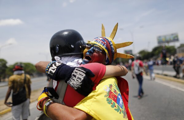 
              An anti-government protester dressed as Lady Liberty, wearing the colors of Venezuela's flag, hugs a fellow protester during a demonstration near La Carlota airbase in Caracas, Venezuela, Wednesday, May 1, 2019. Opposition leader Juan Guaidó is calling for Venezuelans to fill streets around the country Wednesday to demand President Nicolás Maduro's ouster. Maduro is also calling for his supporters to rally. (AP Photo/Ariana Cubillos)
            
