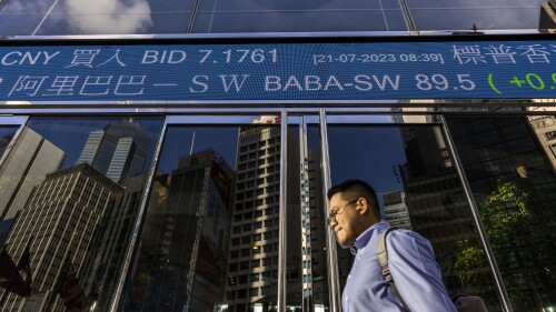 A pedestrian passes by the Hong Kong Stock Exchange electronic screen in Hong Kong, Friday, July 21, 2023. Shares were mixed Friday in Asia after the latest rally on Wall Street fizzled, with big declines for Tesla, Netflix and other big tech-oriented stocks. (AP Photo/Louise Delmotte)