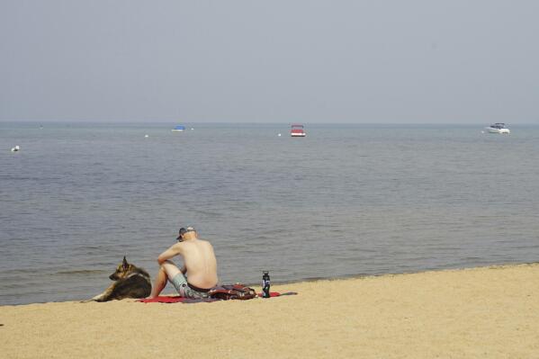 South Lake Tahoe resident Connor Jones sits with his dog on a smoke-cloaked empty beach in South Lake Tahoe, Calif., Monday Sept. 6, 2021. Residents who fled South Lake Tahoe under threat of a wildfire were allowed to return as crews stalled the flames from advancing. (AP Photo/Samuel Metz)