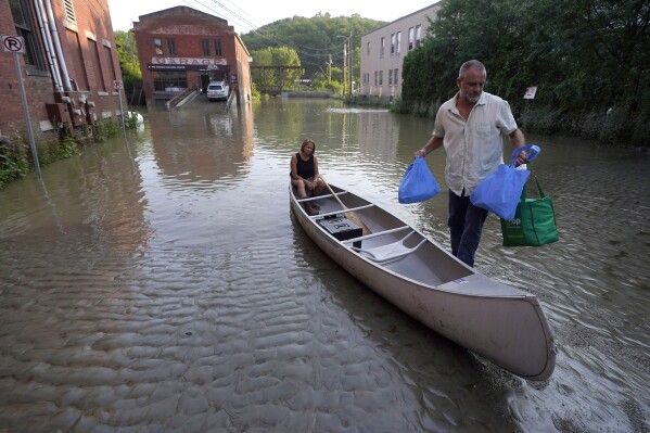 Jodi Kelly, seated center, practice manager at Stonecliff Veterinary Surgical Center, behind, and her husband Veterinarian Dan Kelly, right, use a canoe to remove surgical supplies from the flood damaged center, July 11, 2023, in Montpelier, Vt. The supplies included orthopedic implants for an upcoming surgery on a dog. (AP Photo/Steven Senne)