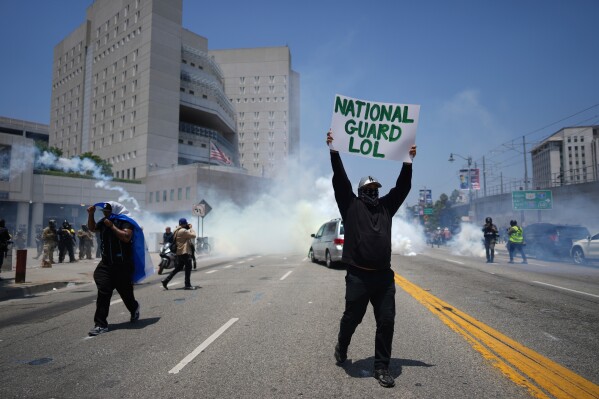 Un manifestante muestra un cartel mientras se utiliza gas lacrimógeno en el centro de detención metropolitano del centro de Los Ángeles, el domingo 8 de junio de 2025, tras la protesta contra la redada migratoria de anoche. (Foto AP/Eric Thayer)