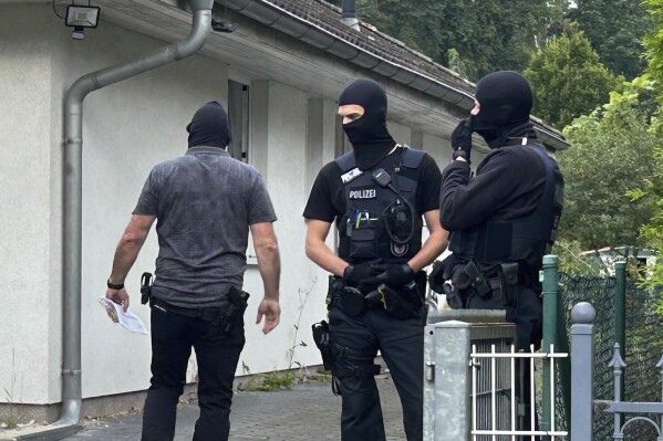 Masked police officers stand in front of a house in falkensee near Berlin, Germany, Tuesday, July 16, 2024. Germany's top security official on Tuesday banned a far-right magazine, accusing it of stirring up hatred against Jews, people with immigrant roots and parliamentary democracy. (Sven Kaeuler/dpa via AP)