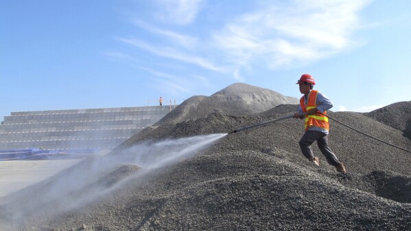 FILE- A Vietnamese worker sprays water over stones to be used in the construction of a silo for storing soil contaminated with Agent Orange dioxide at the site of a former American airbase in Danang, Vietnam on April 24, 2013. (AP Photo/Hau Dinh)