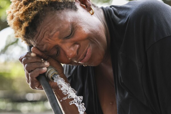 Judy Breland Morris cools off and washes herself off with a hose after she claims she was maced near Jackson Square, during an excessive heat warning in New Orleans, Tuesday, June 27, 2023. (Sophia Germer/The Times-Picayune/The New Orleans Advocate via AP)