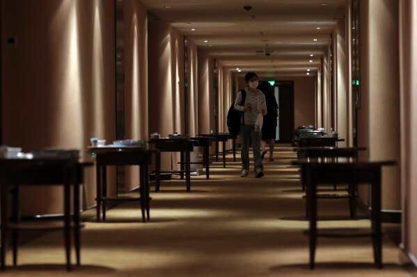 A masked foreign journalist who was selected to cover the opening ceremony of the Chinese People's Political Consultative Conference (CPPCC) walks by breakfast placed on the tables outside each room assigned for journalists in Beijing, Thursday, May 21, 2020. China is strictly limiting the number of journalists who can cover its ongoing legislative session because of the coronavirus outbreak.  (AP Photo/Andy Wong)