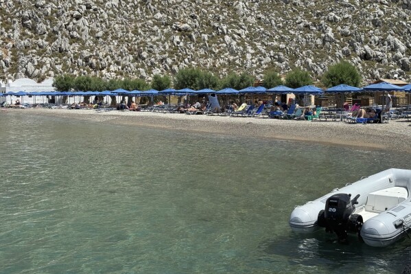 People sit on the beach in Agios Nikolaos on the southeastern Aegean island of Symi, Greece, Friday, June 7, 2024, where British doctor and TV presenter Michael Mosley is believed to have set off from. A massive search and rescue operation still ongoing on the tiny eastern Aegean island of Symi has yet to locate British doctor and TV presenter Michael Mosley, who went missing after going for a walk Wednesday afternoon, Greek police said. (Photo by Associated Press/Antonis Mistiroglou)