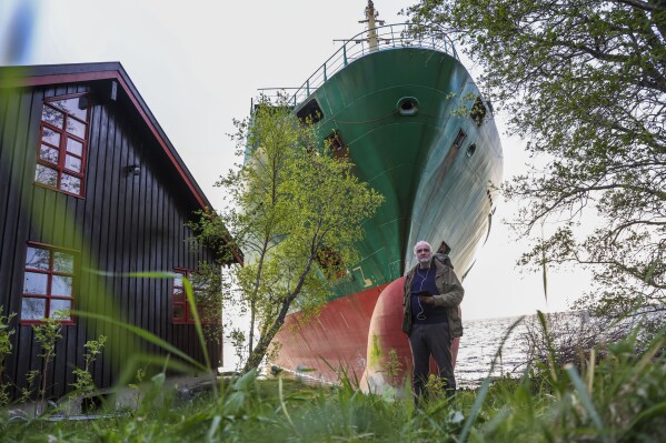Johan Helberg stands next to his house, with the container ship NCL Salten in the background, after the 135-meter-long ship ran aground in the Trondheimsfjord, outside Byneset, in Trondheim, Norway, Thursday May 22, 2025. (Jan Langhaug/NTB Scanpix via AP)