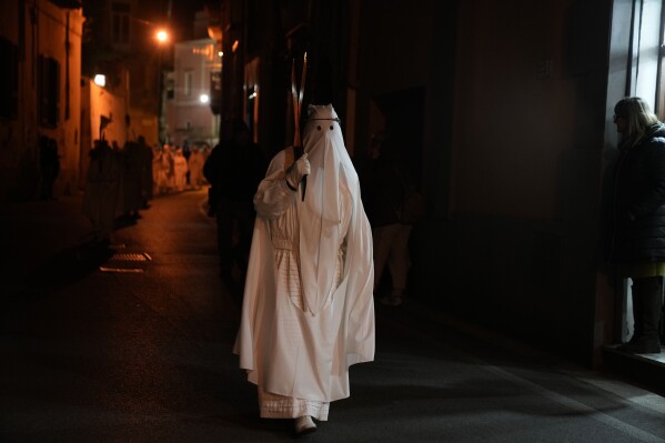 A member of a confraternity carries a cross during a Holy Thursday procession the in Procida Island, Italy, Thursday, March 28, 2024. Italy is known for the religious processions that take over towns big and small when Catholic feast days are celebrated throughout the year. But even in a country where public displays of popular piety are a centuries-old tradition, Procida's Holy Week commemorations stand out. (AP Photo/Alessandra Tarantino)