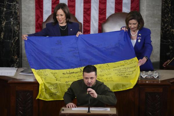 Vice President Kamala Harris and House Speaker Nancy Pelosi of Calif., right, react as Ukrainian President Volodymyr Zelenskyy presents lawmakers with a Ukrainian flag autographed by front-line troops in Bakhmut, in Ukraine's contested Donetsk province, as he addresses a joint meeting of Congress on Capitol Hill in Washington, Wednesday, Dec. 21, 2022. (AP Photo/Jacquelyn Martin)