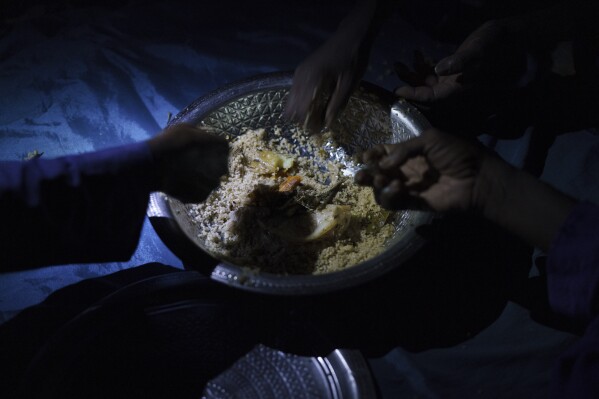 Men share a plate of food during the holy month of Ramadan at a compound of a family of herders in the village of Anndiare, in the Matam region of Senegal, Wednesday, April 12, 2023. (AP Photo/Leo Correa)
