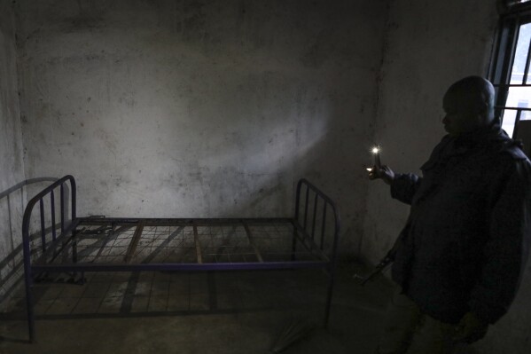 A member of the security forces uses his mobile phone torch to inspect a bedroom inside the Lhubiriha Secondary School following an attack on the school on Saturday, in Mpondwe, Uganda Sunday, June 18, 2023, near the border with Congo. Ugandan authorities have recovered the bodies of 41 people including 38 students who were burned, shot or hacked to death after suspected rebels attacked the school, according to the local mayor. (AP Photo/Hajarah Nalwadda)