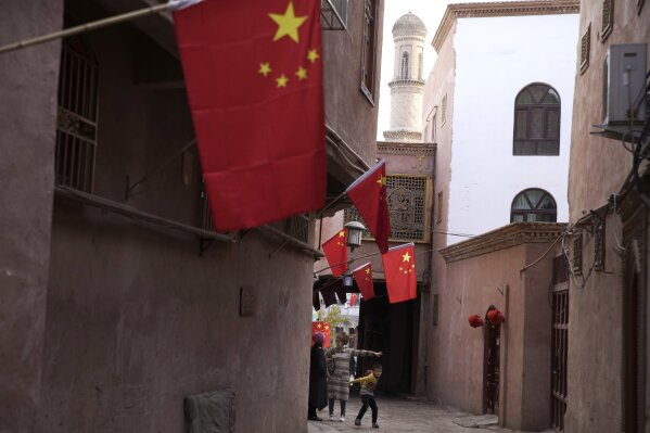
              In this Nov. 4, 2017, photo, a child reacts to a stranger as adults chat along the corridor of the old city district where Chinese national flags are prominently hung in Kashgar in western China's Xinjiang region. Authorities are using detentions in political indoctrination centers and data-driven surveillance to impose a digital police state in the region of Xinjiang and its Uighurs, a 10-million strong, Turkic-speaking Muslim minority Beijing fears could be influenced by extremism. (AP Photo/Ng Han Guan)
            