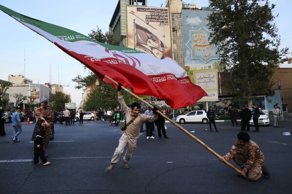 Demonstrators wave a huge Iranian flag in their anti-Israeli gathering in front of an anti-Israeli banner on the wall of a building at the Felestin (Palestine) Sq. in Tehran, Iran, Monday, April 15, 2024. World leaders are urging Israel not to retaliate after Iran launched an attack involving hundreds of drones, ballistic missiles and cruise missiles. The sign on the banner reads in Hebrew: "Your next mistake will be the end of your fake country." And the sign in Farsi reads: "The next slap will be harder." (AP Photo/Vahid Salemi)